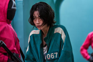 一名身穿青綠色魷魚遊戲制服、編號067的參賽者看起來緊張又害怕。 — 067 魷魚遊戲 壁紙