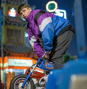年輕男子在霓虹燈照亮的城市夜景中騎著小型摩托車 — 奧利佛樹 壁紙