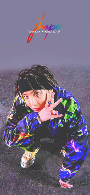 K-pop 藝人 J-Hope 身穿色彩繽紛的服裝蹲下比出和平手勢。 — iPhone 18 壁紙