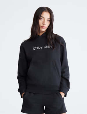 身穿黑色Calvin Klein連帽上衣和短褲、雙手插袋的女性。 — 卡文克萊 壁紙