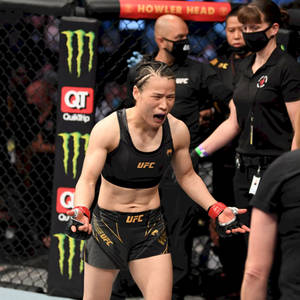 女MMA拳手在UFC八角籠中慶祝勝利，背景有官員。 — 運動 壁紙
