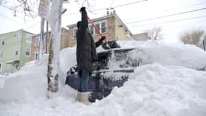 在積雪的街道上，有人正在為汽車剷雪。 — 酷寒冬季 壁紙