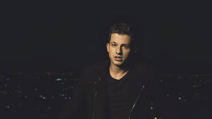 年輕男子身穿黑色外套，以城市夜景為背景 — 查理·普斯 壁紙