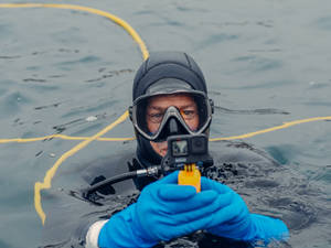 潛水員手持GoPro相機在水面上方，身後拖著黃色繩索 — 攝影 壁紙