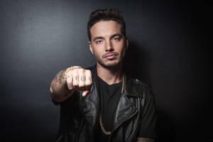 身穿黑色皮夾克的男子，帶有紋身和金飾，將拳頭指向鏡頭。 — J Balvin 壁紙