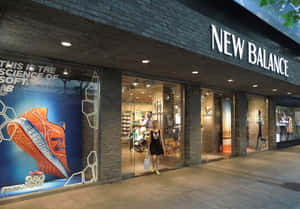 女子在夜晚走過New Balance鞋店，櫥窗上有巨大的橙色運動鞋廣告。 — New Balance 壁紙