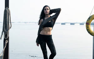 身穿黑色運動服的女性在日落時分於海濱碼頭旁擺姿勢。 — Shraddha Kapoor 壁紙