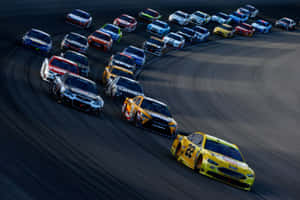 NASCAR賽車在日落時分沿彎曲賽道飛馳。 — 汽車 壁紙