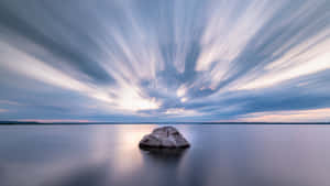 在帶有條紋的暮色天空下，平靜水面上的一塊孤獨岩石。 — 海景 壁紙