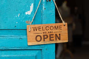 一塊寫有 welcome we are open 的木牌掛在藍色的門上。 — MacBook Pro M4 壁紙