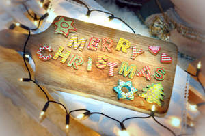 薑餅餅乾在木板上拼出 Merry Christmas，配有燈串。 — 可愛聖誕快樂 壁紙