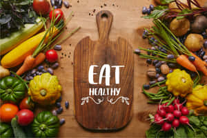 新鮮蔬菜和香草圍繞著一塊帶有「EAT HEALTHY」字樣的木製砧板擺放。 — 水果 壁紙
