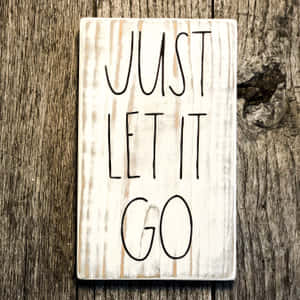 一塊木牌，上面寫有「Just Let It Go」字樣，背景為質樸的木紋。 — うちはイズミ 壁紙