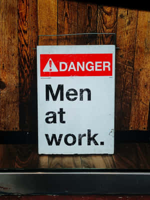 一塊磨損的警告標誌，上面寫著「Men at work」，安裝在木牆上。 — 2048x2732 壁紙