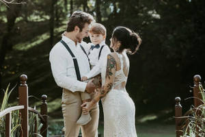 一家三口在陽光照耀的森林中的木橋上擁抱。 — 婚紗 壁紙