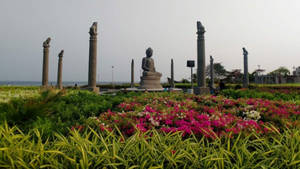 佛像 surrounded by 色彩繽紛的花朵和石柱 near 海洋。 — 海德拉巴 壁紙