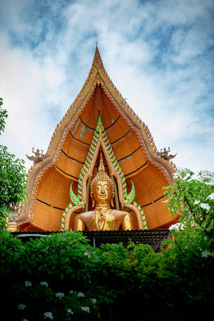 金色佛像在裝飾寺廟屋頂下，被綠色植物和雲朵環繞。 — 佛陀 壁紙