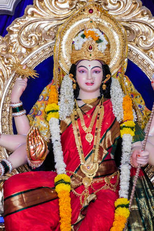 一尊裝飾華麗的印度教女神雕像，身穿紅金色服飾，配有花環。 — Maa Durga 壁紙