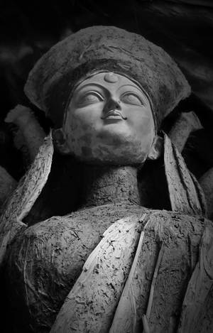 風化佛像特寫，頭戴皇冠，身披垂褶長袍，黑白呈現。 — Maa Durga 壁紙