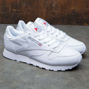 白色Reebok運動鞋，帶紅色和藍色細節，在灰色混凝土上，靠近木頭。 — 銳步 壁紙