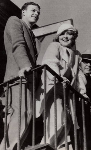 一對穿著1930年代服裝的男女在陽台欄杆上微笑。 — 克拉拉·鮑 壁紙