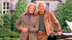 一對老年夫婦快樂地在復古敞篷車旁擺姿勢。 — Ralph lauren 壁紙