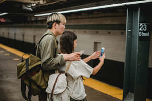一對情侶站在地鐵月台上一起看著手機。 — 可愛情侶 壁紙