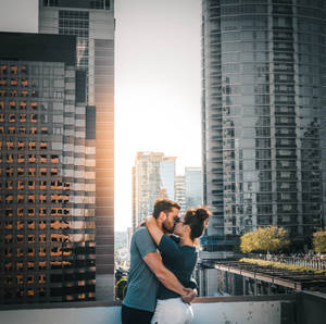 情侶在天臺上接吻，背景是夕陽下的城市天際線 — 情侶 壁紙