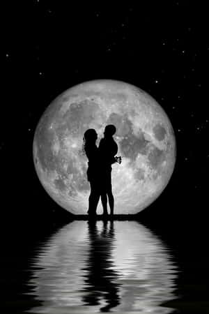 一對情侶以剪影形式在夜間水面倒映的滿月下擁抱。 — 美學月亮 壁紙