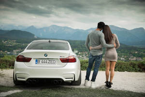 情侶在白色BMW M4附近擁抱，俯瞰群山。