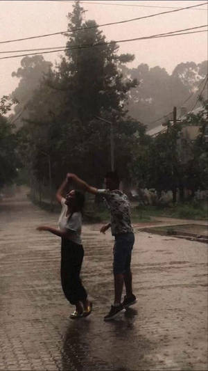 兩個人在雨中，在濕漉漉的街道上跳舞，背景有樹木。 — 情侶 壁紙