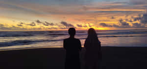 沙灘上情侶剪影觀賞海上多彩夕陽 — 海灘日落 壁紙