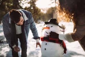 一對情侶在日落時分的雪地森林中堆雪人。 — 酷寒冬季 壁紙