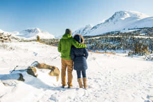 情侶站在雪中，互相擁抱，面向雪山。 — 酷寒冬季 壁紙