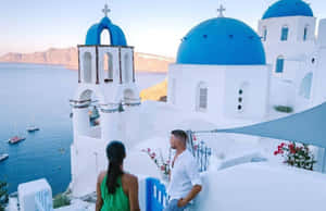 情侶在聖托里尼日落時欣賞藍頂教堂和海景。 — 雅典 壁紙