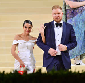穿著正式服裝的夫婦在大樓梯活動上揮手。 — 艾瑪·羅勃茲 壁紙