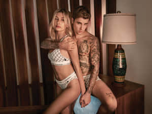 紋身情侶穿著Calvin Klein內衣，在裝飾燈具的木質房間裡擺姿勢。 — 卡文克萊 壁紙