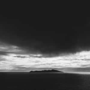 在黑暗暴風雨的天空下，一個小島孤獨地矗立在海洋中。 — iPad 第10代 壁紙