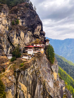 一座懸崖邊的修道院，高高棲息在岩石山上，下方是森林覆蓋的山谷。 — 不丹 壁紙