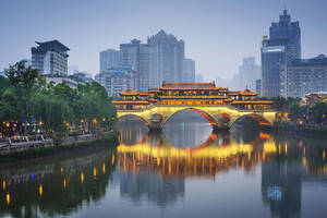 黃昏時分亮燈的歷史中國橋樑，河中有倒影，周圍是城市建築。 — 塔橋 壁紙
