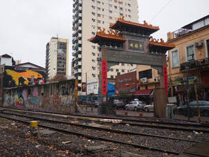 城市環境中的中式牌坊，帶有塗鴉和火車軌道，天空灰暗 — 布宜諾斯艾利斯 壁紙