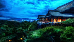 一座發光的日本寺廟在暮色中隱藏在綠樹之間，俯瞰城市。 — 山脈 壁紙
