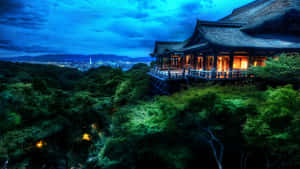 一座發光的寺廟隱藏在綠樹中，俯瞰著暮色中的城市。 — 日本 壁紙