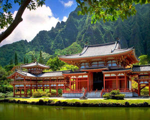 池塘旁的紅色木造寺廟，背景有翠綠山巒