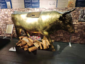 金色公牛雕像，下方有圓木和火，在博物館環境中。 — 金色 壁紙