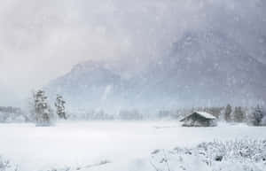 冬季風景中的雪中小屋，有山脈和飄雪。 — 冬季風景 壁紙