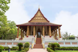 一座金色和紅色的寺廟，周圍環繞著綠樹和白色柵欄，在藍天下。 — 博物館 壁紙