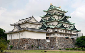 一座歷史悠久的日本城堡，白色牆壁和綠色屋頂，被石牆和綠樹環繞。 — 京都 壁紙