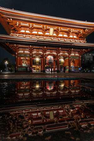 夜晚水坑中倒映的燈火通明的日本寺廟大門。 — 黑色 壁紙