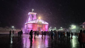 雪夜中閃爍著粉紅色燈光的寺廟，人們聚集在外面。 — 金廟 壁紙